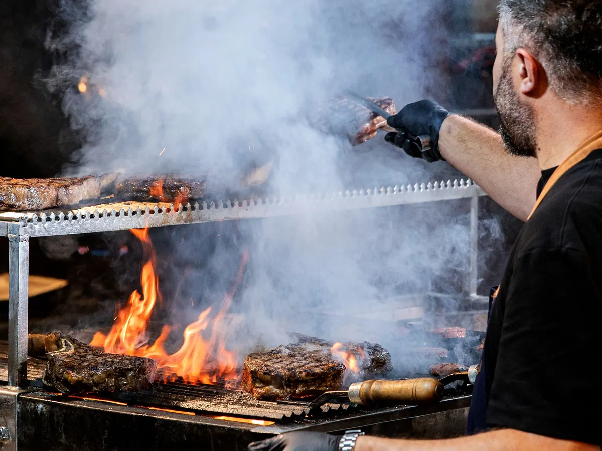 Grillmeister wendet Steaks über offenem Feuer