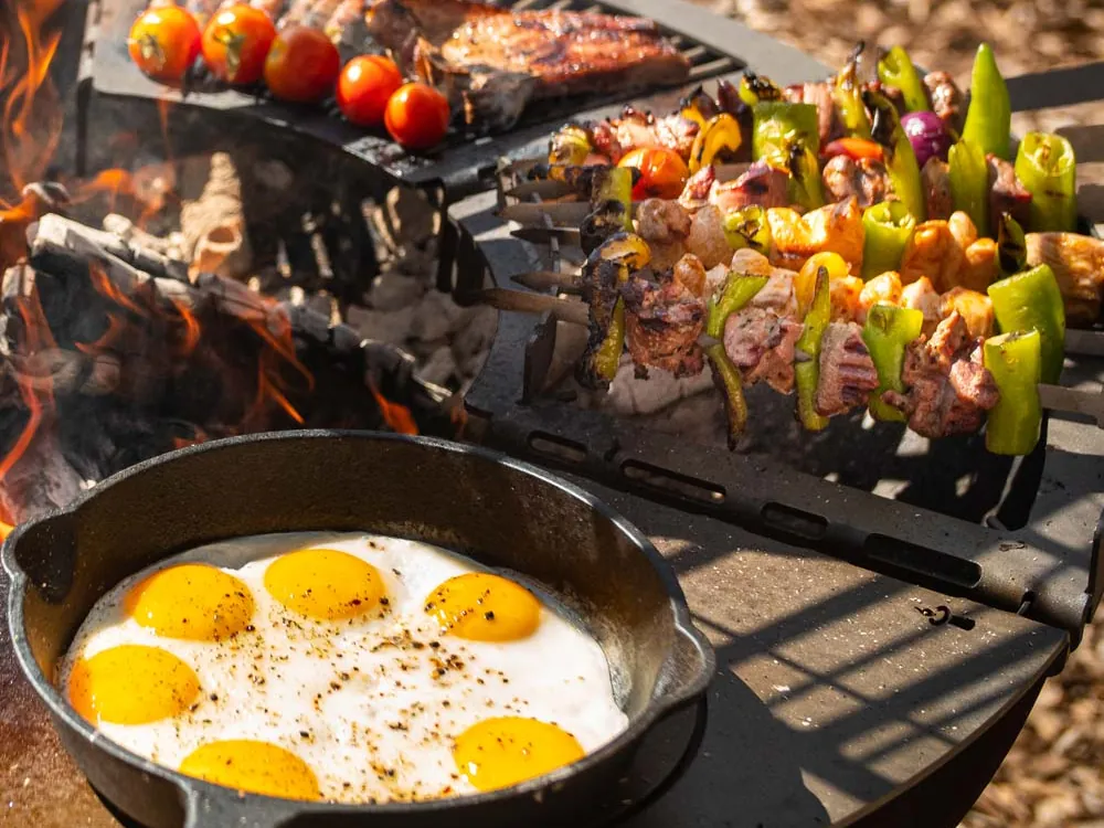 Nahaufnahme der Remundi Grillmodule: Spieß-Modul, Grillrost mit Tomaten und Steaks, gusseiserne Pfanne mit Spiegeleiern